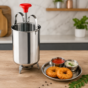 A stainless steel medu vada maker with a red handle stands next to a plate of vadas and two dipping sauces.