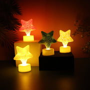 Four glowing star-shaped LED tealight candles in red, green, and two yellow, on dark and light blocks.