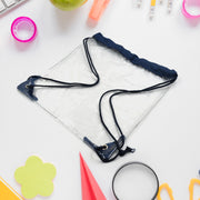 Clear drawstring bag with dark blue cords and accents, lying on a white desk surrounded by school supplies.
