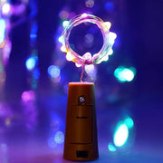 A single bottle cork light with a coiled string of multi-color LEDs glowing brightly against a blurred purple background.
