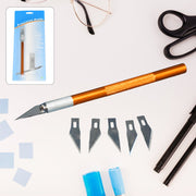 Orange precision knife, five blades, and product packaging on a light desk with glasses and scissors.