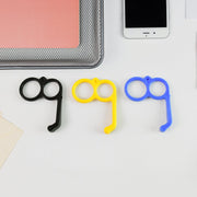 Three plastic finger ring phone holders in black, yellow, and blue on a white desk.