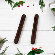 Two brown anti-slip eyeglass ear grips on a white wooden background with sparse green foliage and red berries.