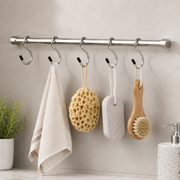 Five S-shaped hooks hang from a silver bar, holding a towel, sponge, pumice stone, and brush.
