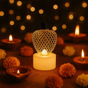 A single glowing gold mesh LED tealight surrounded by traditional clay diyas and orange marigold flowers, with bokeh lights