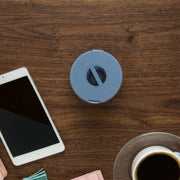 A closed blue cable winder case is centered on a wooden desk with a tablet and coffee cup.