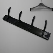 Black four-hook coat rack mounted on a light wall, with a dark wooden clothes hanger visible above it.