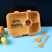 Closed yellow 4-compartment lunch box with clear lid and orange cutlery, on a blue surface with a flower.