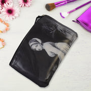 Black cosmetic bag with a classical portrait, on a white surface with pink flowers and purple brushes.