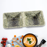 A speckled gray-green ceramic two-compartment serving dish on a white surface with food items.