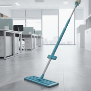 A blue and silver flat mop cleans a grey office floor, with desks and windows in the background.