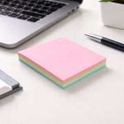 A stack of pink, yellow, and blue sticky notes on a white desk next to a laptop and a black pen.