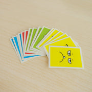 A fan of colorful cards, each depicting a different facial expression, is spread out on a light wooden surface.