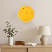 A yellow round wall clock hangs above a wooden console table with a plant, a wooden box, and a lamp.