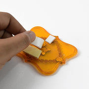 A hand applying white adhesive foam squares to the back of a yellow Shubh Labh wall hanging.