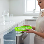 A woman placing a green oval silicone ice cube tray with ice into a stainless steel freezer drawer.