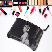 Black cosmetic bag with a classical portrait, surrounded by various makeup palettes and brushes on white.