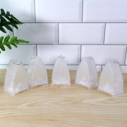 Five clear plastic ribbed lanterns with metal hooks on top, arranged on a light wooden surface against white subway tiles.