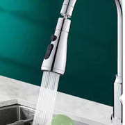 A chrome faucet sprayer head with black buttons sprays a strong stream of water into a sink with a green object.