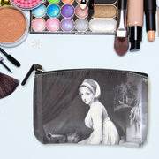 Black cosmetic bag with a classical portrait, on a light blue surface surrounded by makeup items.