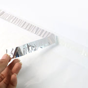 A hand peeling the silver adhesive strip off a clear polybag on a white background.