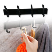 Black four-hook coat rack on a grey tiled wall, with a hand holding a loofah and a grey towel hanging.