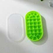 A green oval silicone ice cube tray and its clear lid, both with water droplets, on a white countertop.