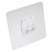 A clear square self-adhesive wall hook with two transparent prongs is shown against a plain white background.