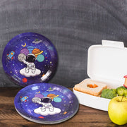 Two purple paper plates with an astronaut and planets design, next to an open lunchbox and an apple.