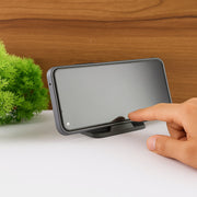 A hand touches the screen of a smartphone resting horizontally on a black mobile stand, next to a green plant.