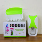 The white and lime green automatic toothpaste dispenser, toothbrush holder, and product packaging box on a wooden surface.