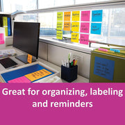 An office desk with a computer monitor, various office supplies, and colorful sticky notes attached to a clear partition and