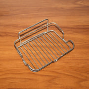 A stainless steel wire soap dish is angled on a dark wood surface, highlighting its wire construction.