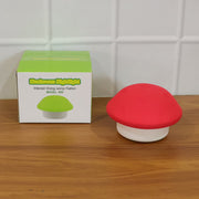 Red and white mushroom night light next to its green-themed product box on a wooden surface.
