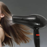 A black hair dryer blows air onto a woman's long, brown hair, showing the hair flowing from the airflow.