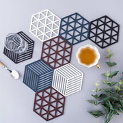 An overhead view of multiple hexagonal and square silicone coasters in various colors, with a teacup and glass.