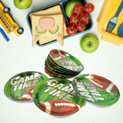 A stack of green football-themed paper plates with four individual plates, surrounded by school lunch items.