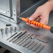 A hand uses an orange flexible bit extension with a drill to fasten a screw into a metal frame, surrounded by various bits.