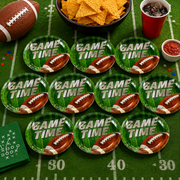 Ten green paper plates with a football and 'GAME TIME' text, surrounded by football-themed party items.