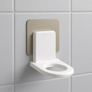 A white plastic wall-mounted bottle holder with a metallic adhesive backing on a white tiled wall.