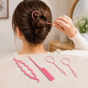 A person uses a pink loop tool to create a bun, with other pink plastic styling tools on a beige surface.