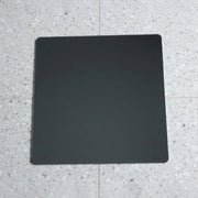 A square mirror with rounded corners lies flat on a speckled gray and white tiled floor.