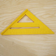 A yellow plastic speed square ruler with black markings is placed on a light wood grain surface.