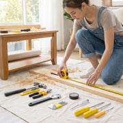 A person in denim overalls measures a wooden board with a yellow tape measure, surrounded by various hand tools.