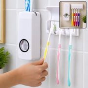 A hand holds a yellow toothbrush to the dispenser, with three other toothbrushes hanging in the holder.