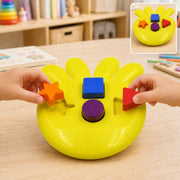 Two children's hands place orange star and red triangle shapes into a yellow shape sorter on a wooden table.