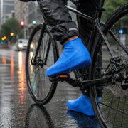 A person on a bicycle wears blue waterproof shoe covers on a wet city street