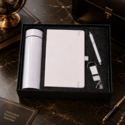 White thermal bottle, notebook, pen, and keychain in a black gift box on a dark marble surface.