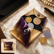 An open iridescent coin pouch with purple and gold hues holds several Indian coins on a marble surface.