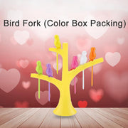 A yellow tree holder with colorful bird fruit forks on a wooden surface with a pink heart-patterned background.
